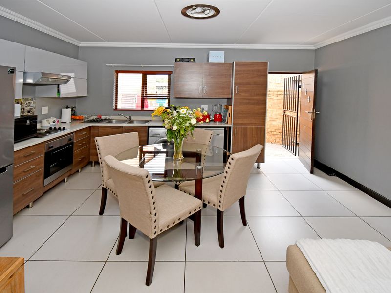 Modern open-plan kitchen and dining area featuring contemporary cabinetry, integrated appliances, tiled flooring, and direct access to an outdoor space.