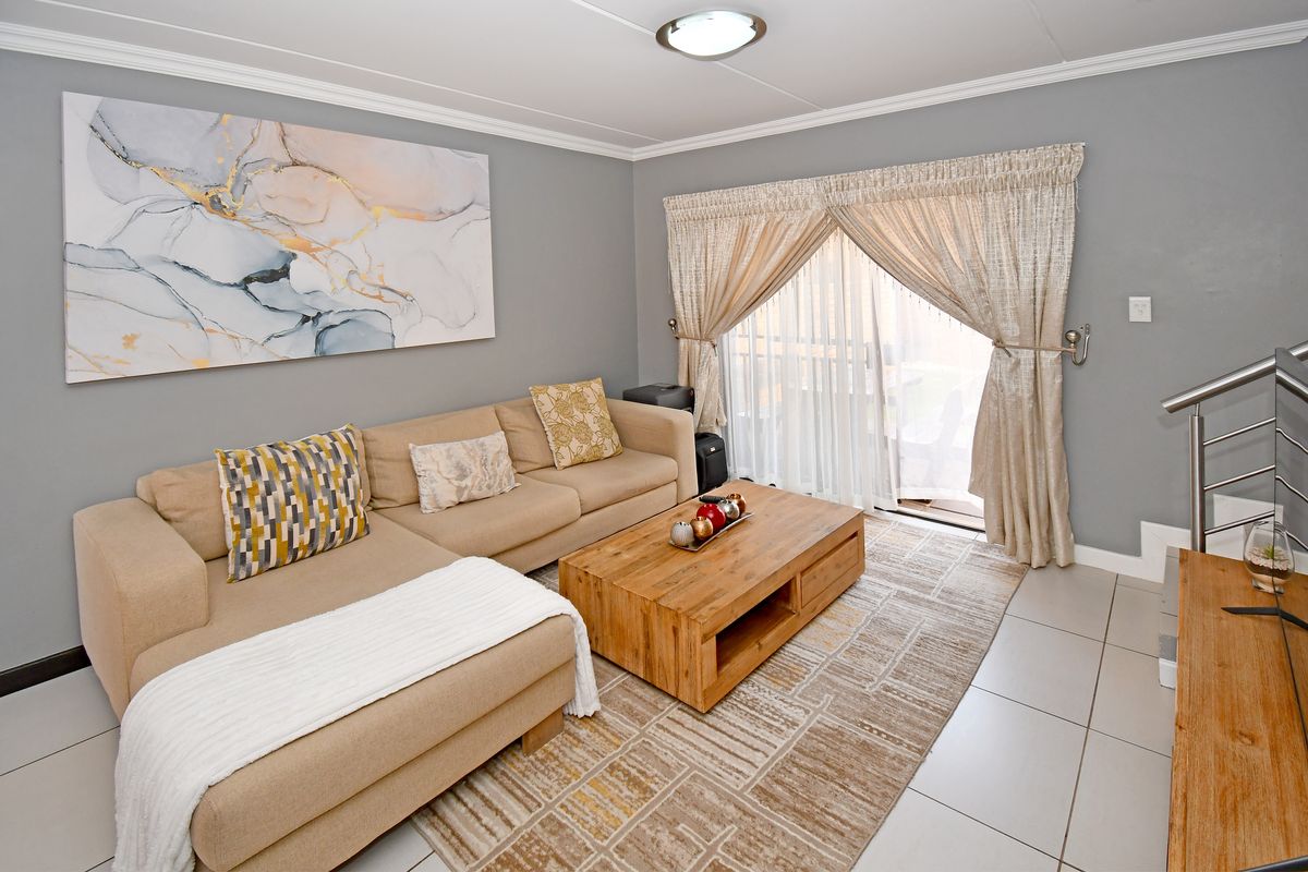 A well-maintained living room featuring neutral tiled flooring, crown molding, and a sliding glass door providing access to the outdoor area.