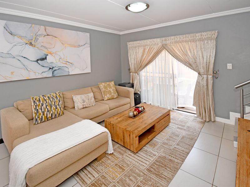 A well-maintained living room featuring neutral tiled flooring, crown molding, and a sliding glass door providing access to the outdoor area.