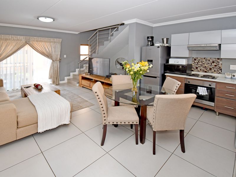 Open-plan living and dining area featuring a modern kitchen with built-in appliances, tiled flooring, and a staircase leading to the upper level.