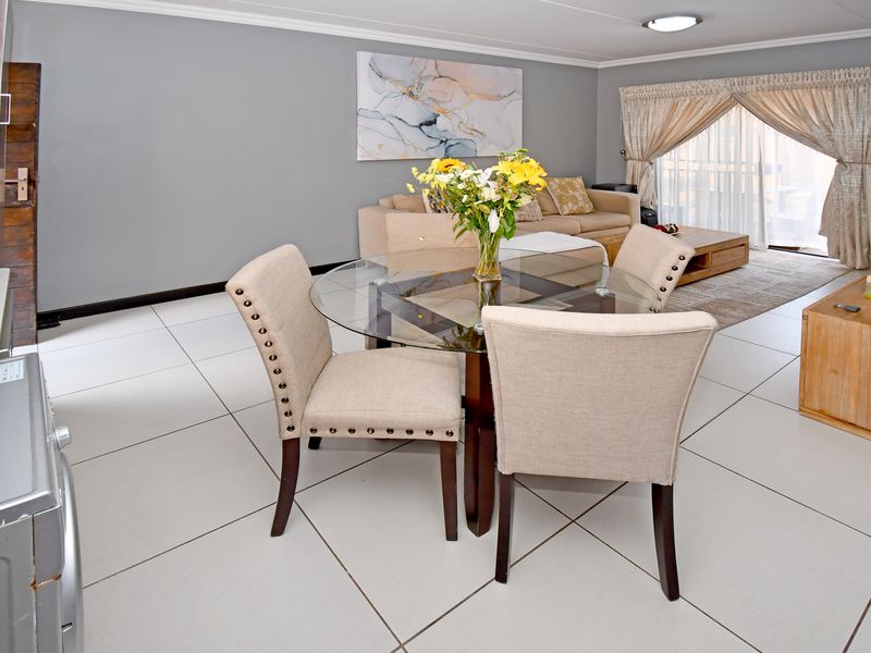 An open-plan living and dining area featuring neutral tiled flooring, grey walls, and a sliding glass door providing access to the exterior.