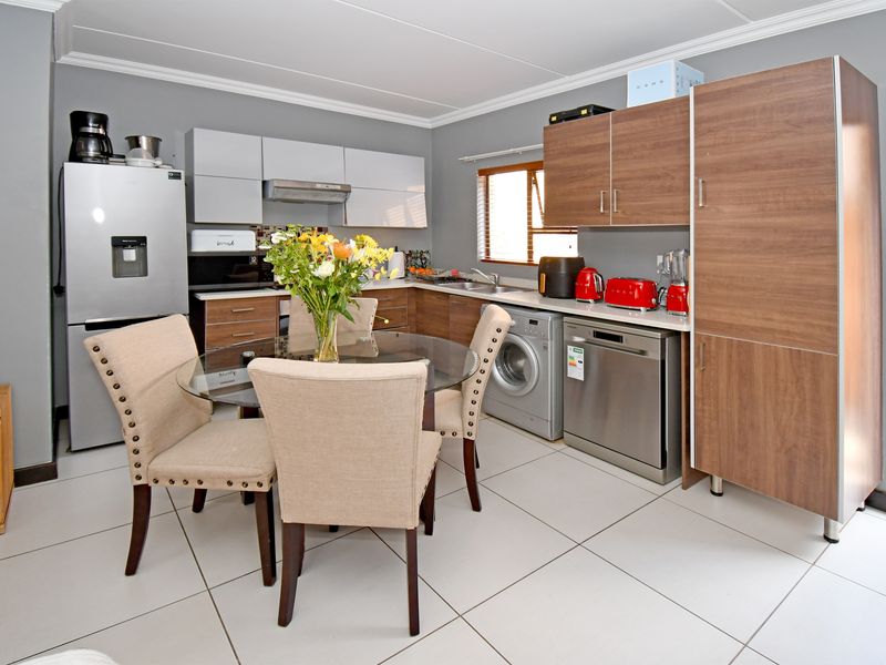 A functional kitchen featuring modern wood-tone and grey cabinetry, tiled flooring, integrated dishwasher, and built-in laundry facilities, offering a practical and well-organized workspace.