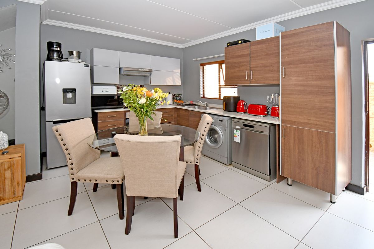 A functional kitchen featuring modern wood-tone and grey cabinetry, tiled flooring, integrated dishwasher, and built-in laundry facilities, offering a practical and well-organized workspace.