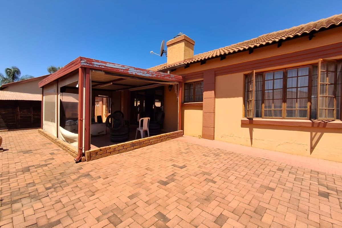 Rear view of the house featuring a covered patio area with brick paving and a tiled roof structure.