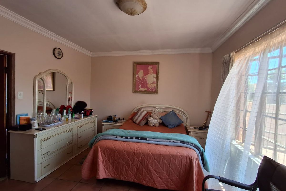 A bedroom featuring tiled flooring, ceiling cornice detailing, and a window fitted with security bars, providing a functional and lived-in space.
