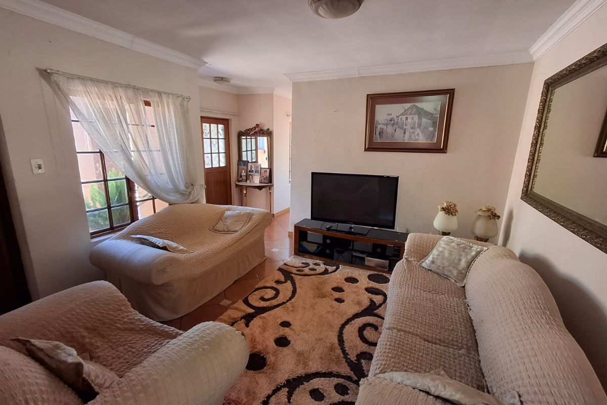 A comfortable living room featuring tiled flooring, ceiling cornicing, and natural light through a window, providing a functional and inviting space.