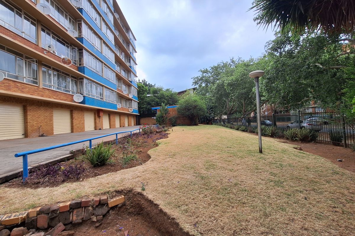 Exterior view of the apartment building featuring a rear garden area, brick facade, and row of garage doors.