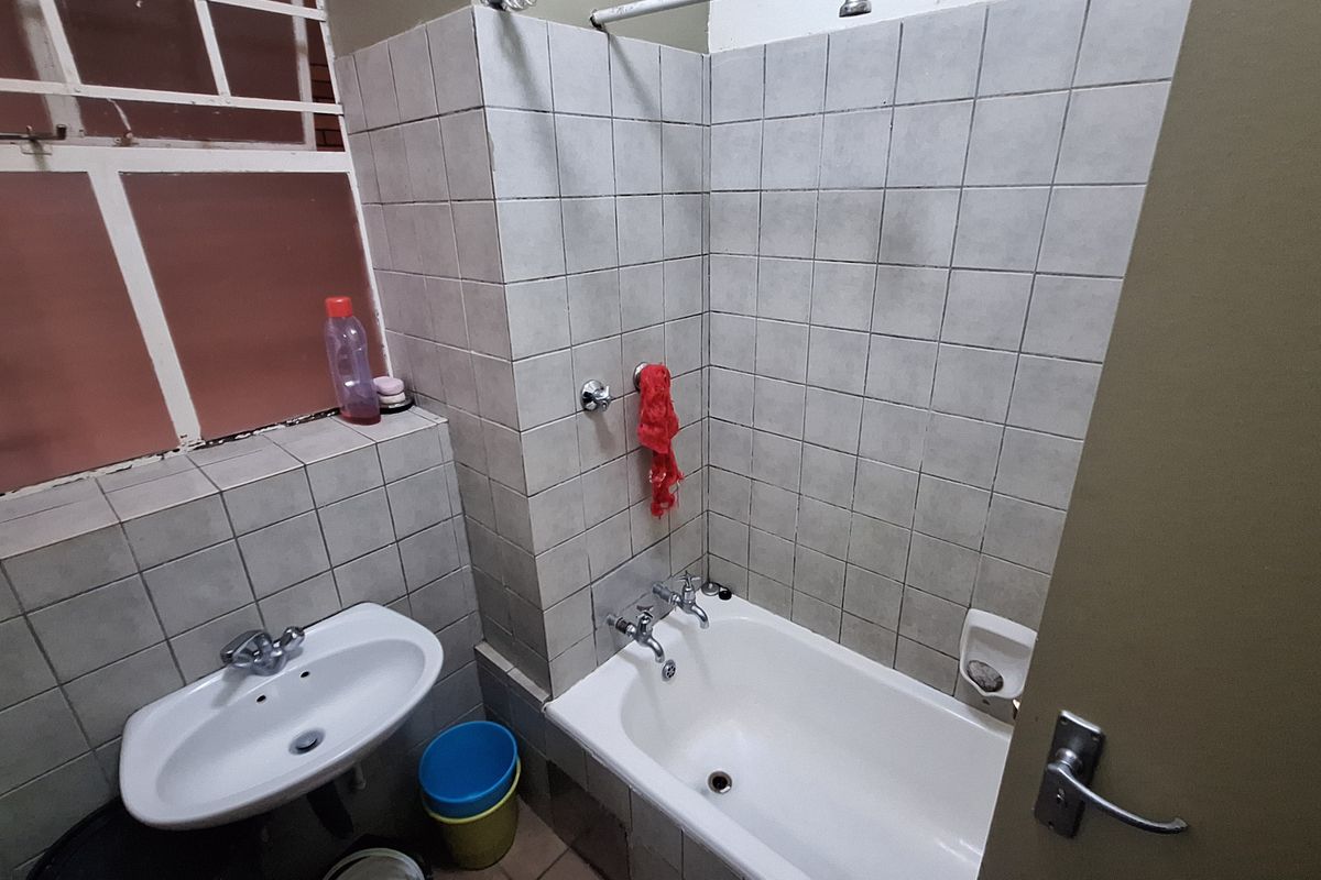 A functional bathroom featuring a bathtub, wall-mounted basin, and tiled finishes, requiring cosmetic updates to improve its overall condition and aesthetic appeal.