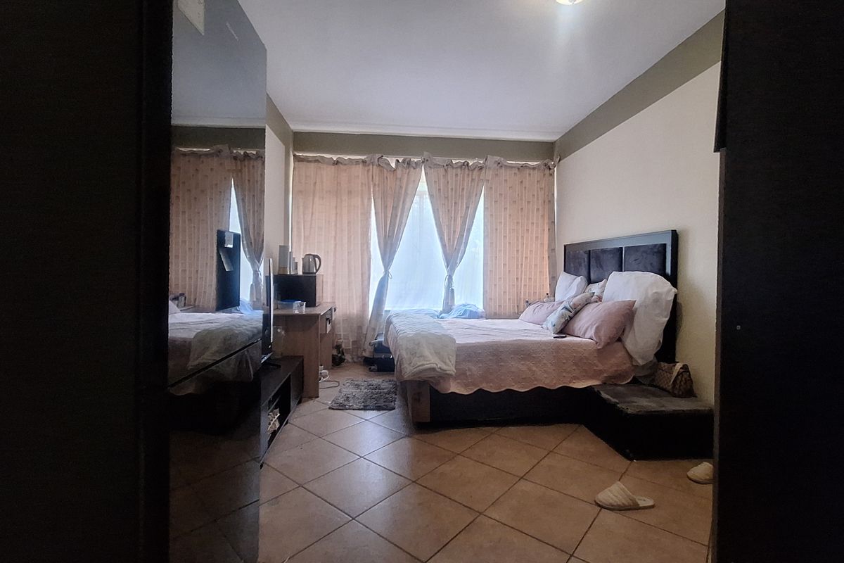 A bedroom featuring tiled flooring and large windows with curtain rails, offering a functional space with neutral wall tones.