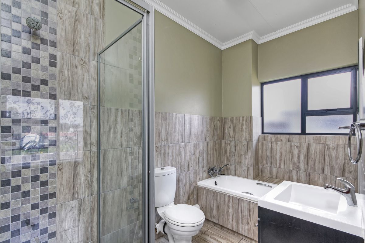 A modern bathroom featuring a glass-enclosed shower, a built-in bathtub with wood-look tiling, a toilet, and a vanity basin.