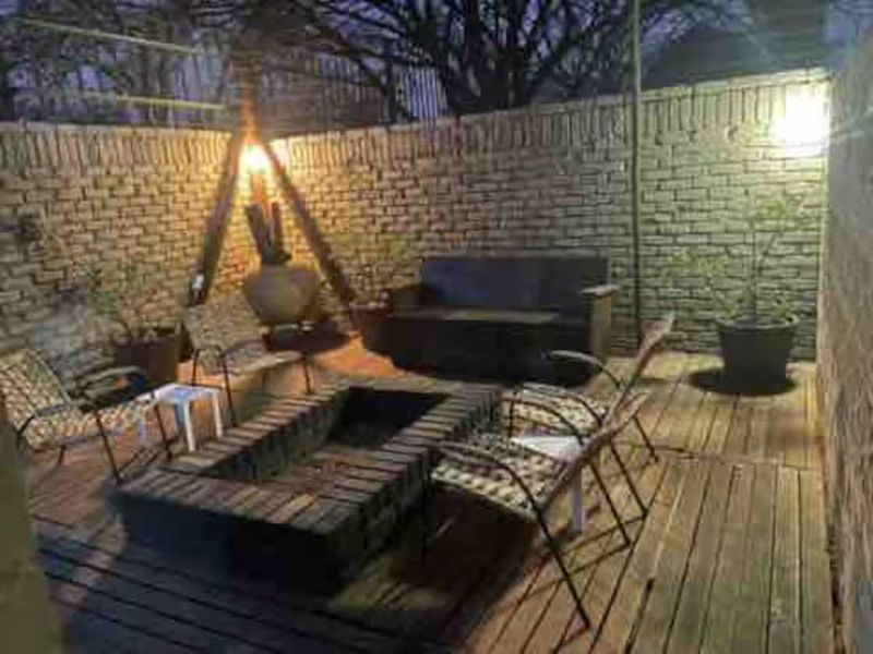 An outdoor patio area featuring timber decking, a built-in brick fire pit, and enclosed by a brick boundary wall.