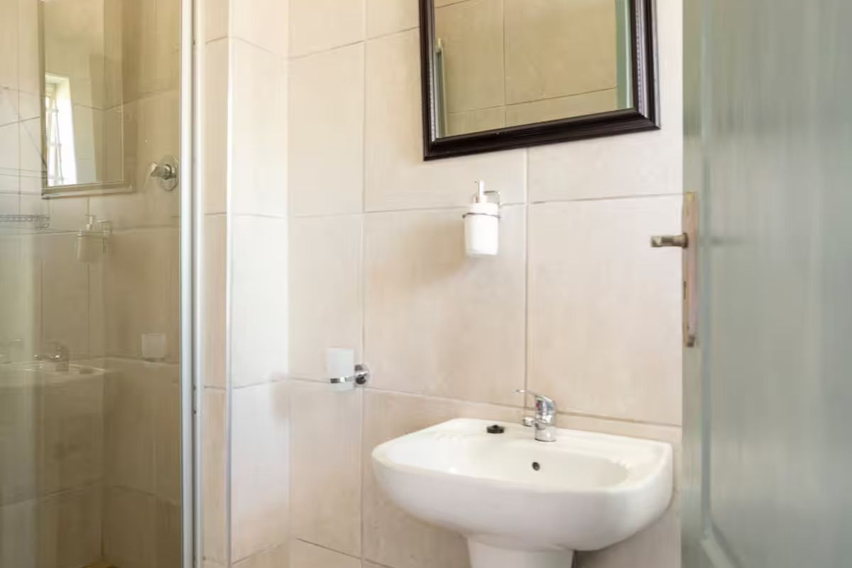 A clean and functional bathroom featuring a pedestal basin, tiled wall finishes, and a glass-enclosed shower unit.