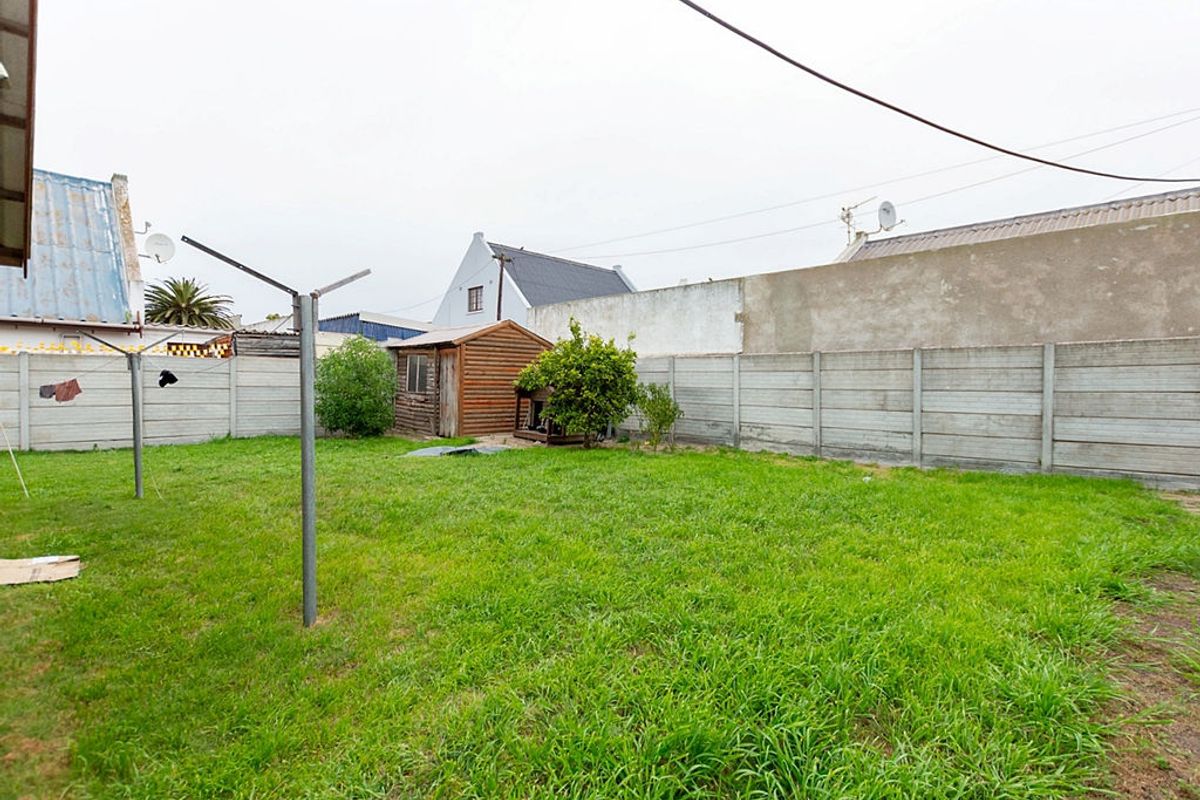 A spacious rear garden featuring a large lawn area, enclosed by precast concrete boundary walls and including a small wooden storage shed.