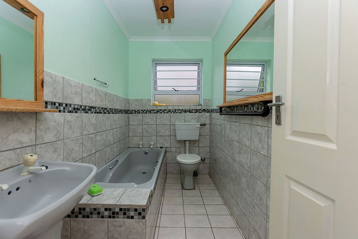 A functional bathroom featuring a built-in bathtub, pedestal sink, toilet, and tiled walls with a decorative border.
