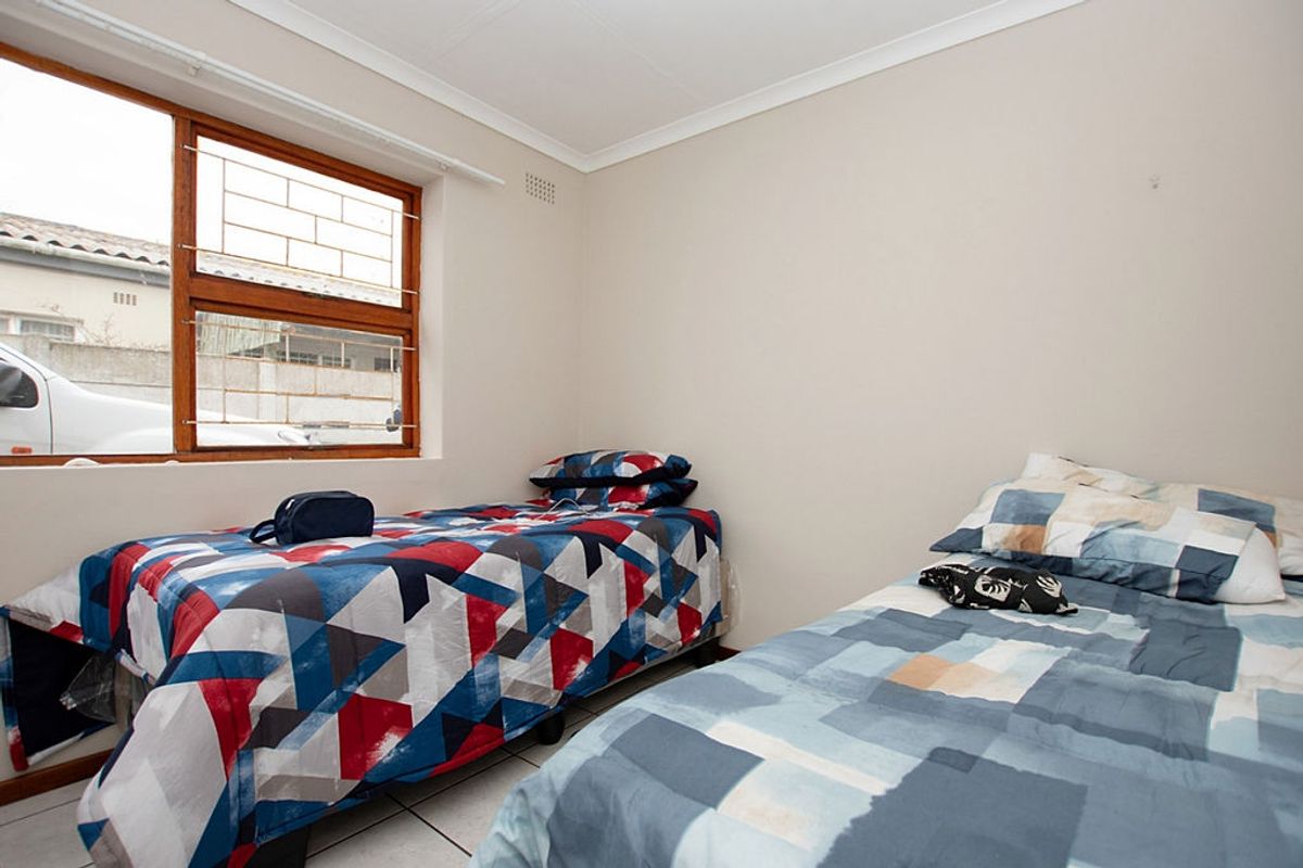 A functional bedroom featuring tiled flooring, a large window with security bars, and neutral wall finishes.
