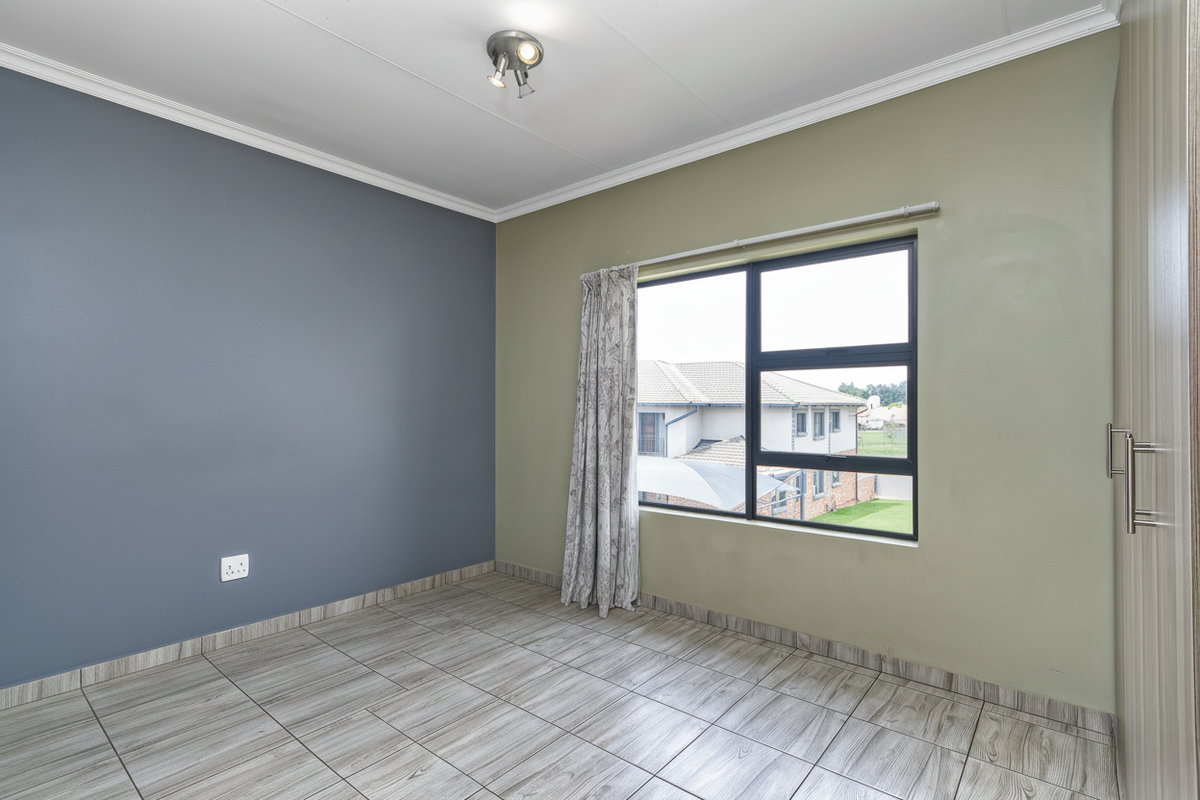 A bright bedroom featuring wood-look tiled flooring, built-in cupboards, and dual-tone painted walls with a large window providing natural light.