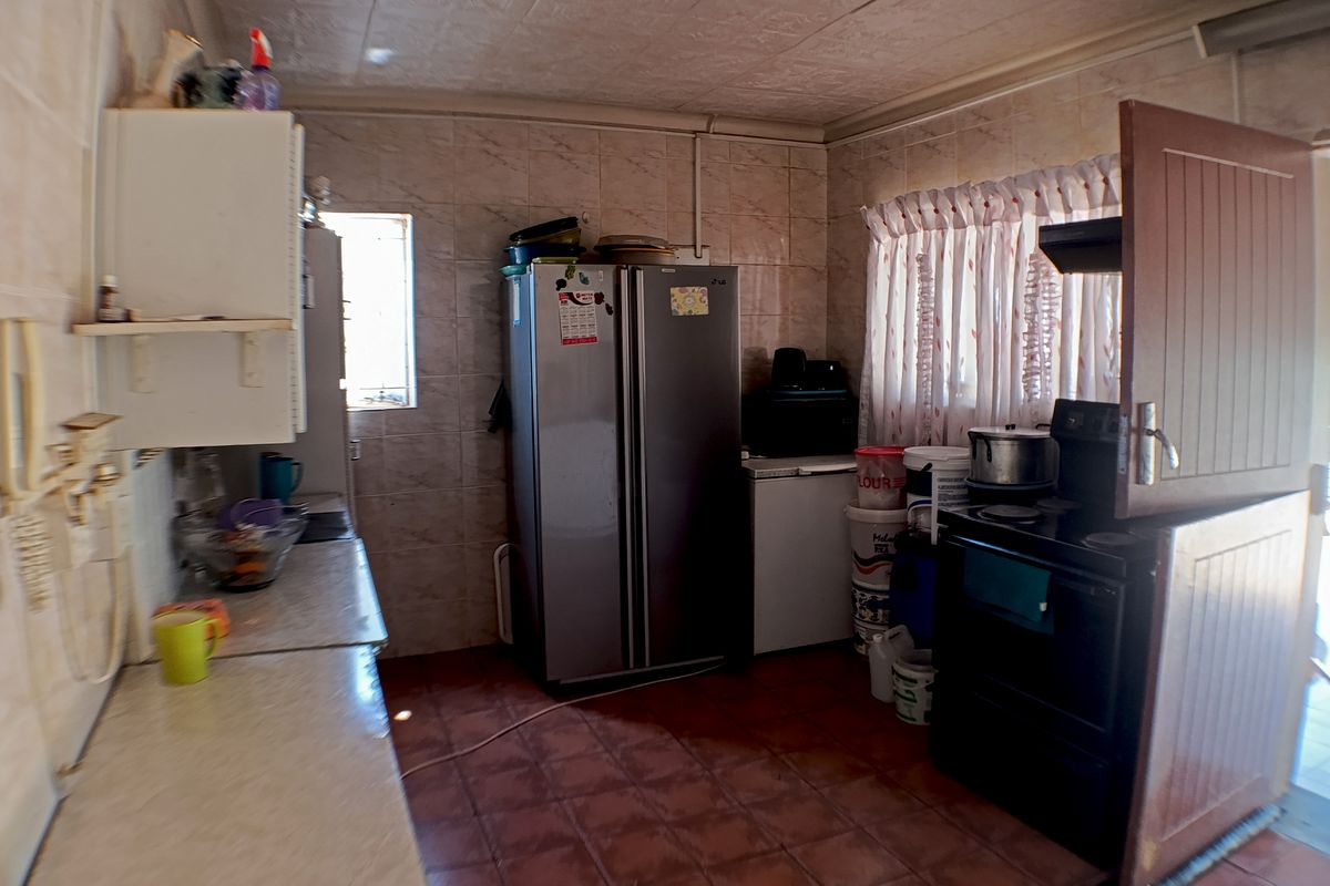 A functional kitchen featuring tiled walls and flooring, equipped with a built-in stove, extractor fan, and cabinetry, with direct access to an outdoor area.