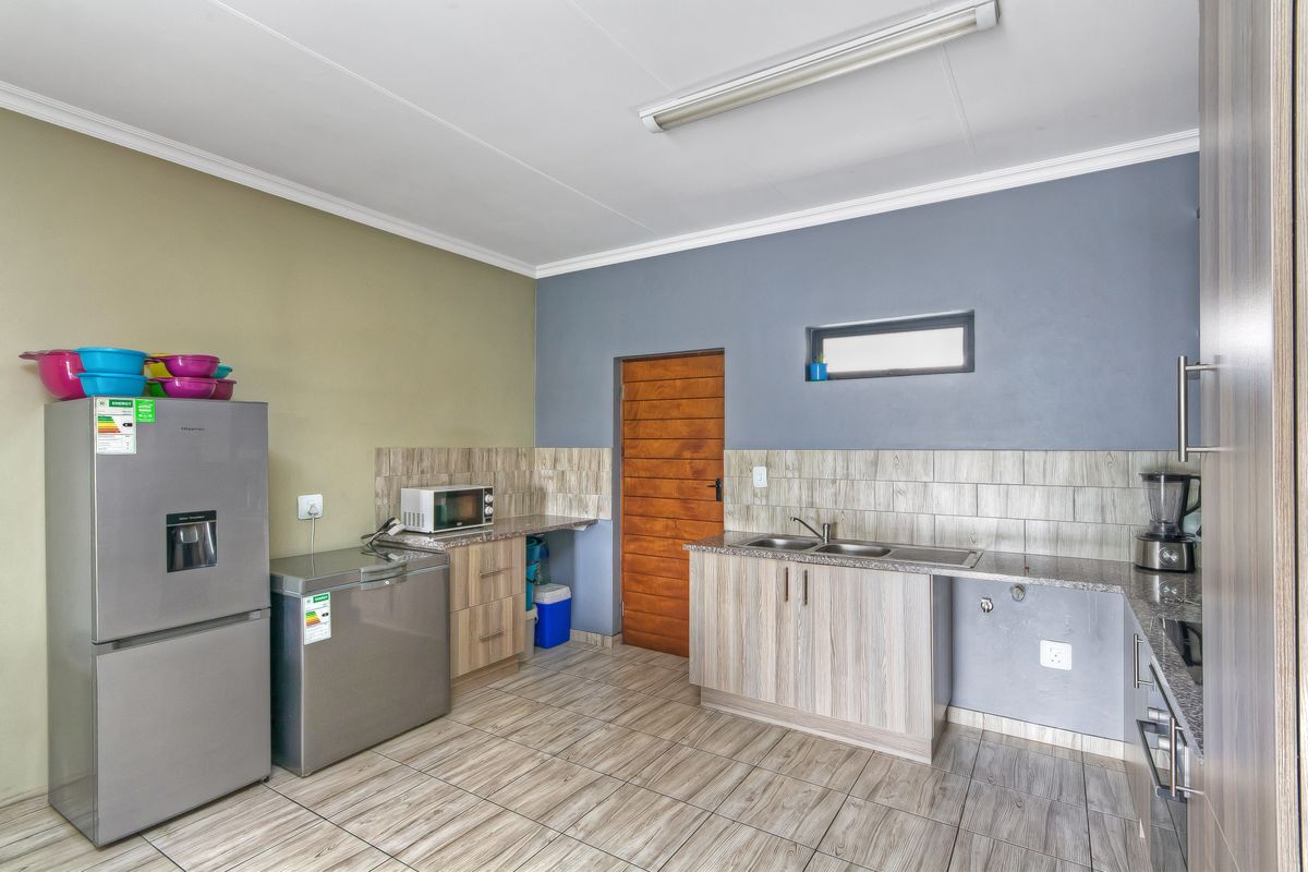 A functional kitchen featuring wood-look cabinetry, granite-style countertops, tiled flooring, and a double-basin sink with integrated plumbing.