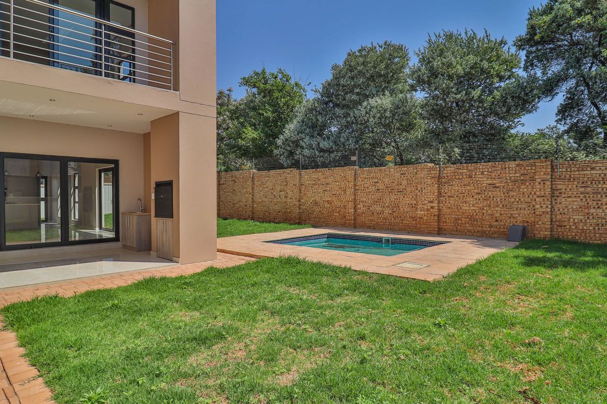 Rear garden featuring a paved patio, built-in braai, swimming pool, and a secure brick boundary wall with electric fencing.