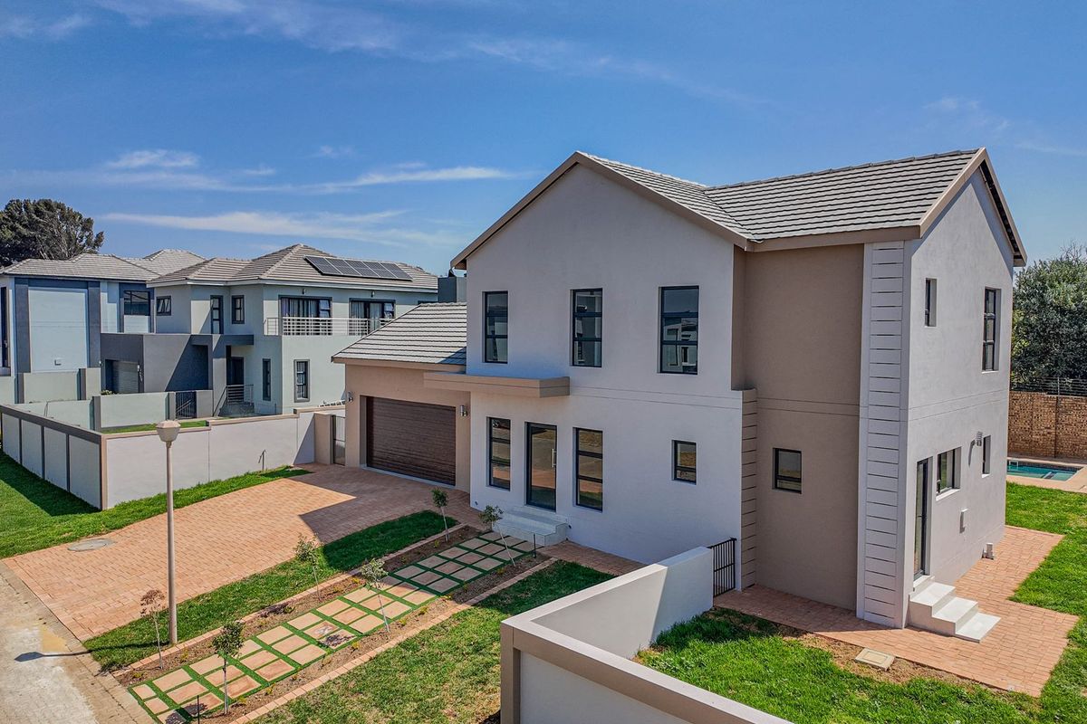 Aerial view of a modern two-story residential property featuring a paved driveway, double garage, landscaped garden, and a private swimming pool.