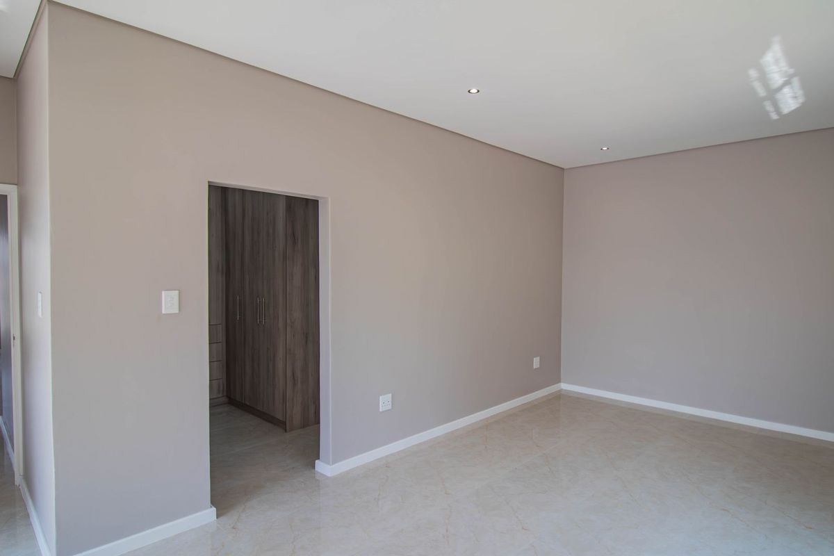 A spacious, modern bedroom featuring neutral walls, polished tiled flooring, recessed lighting, and an adjoining walk-in closet with built-in cabinetry.