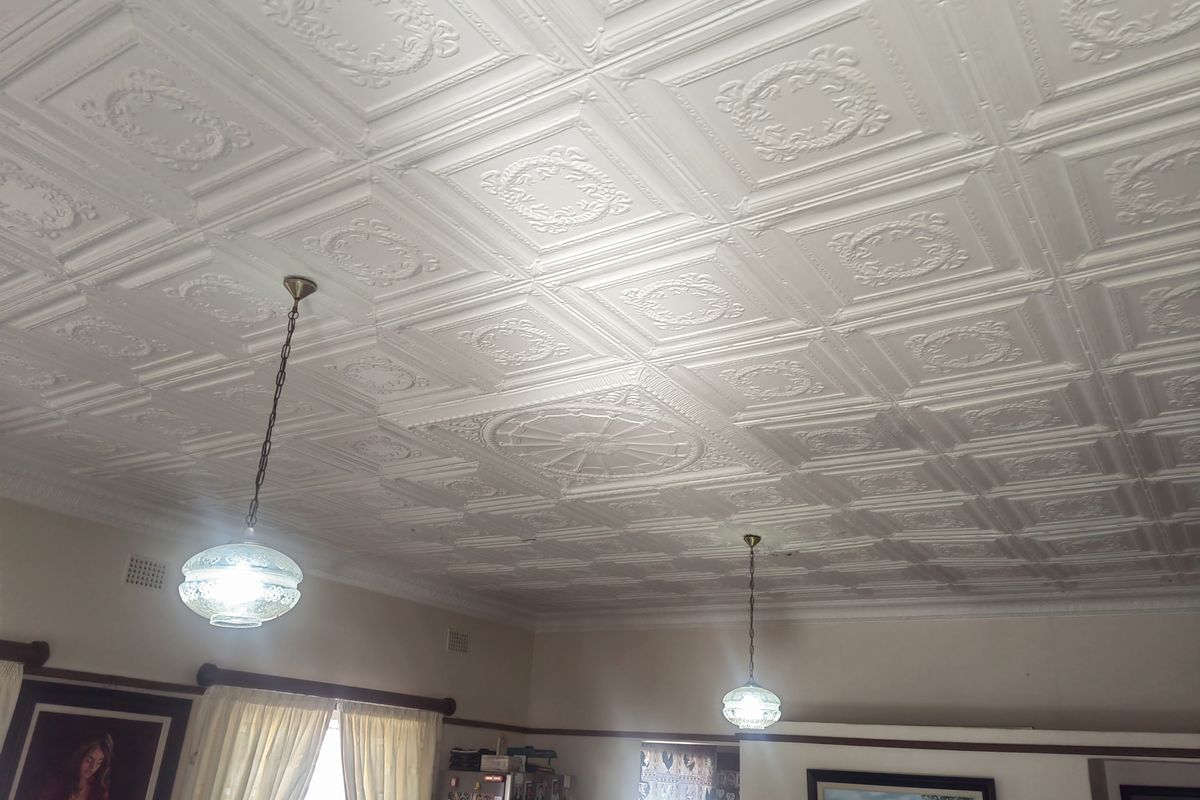 A living area featuring a classic ornate pressed metal ceiling with decorative ceiling roses and period-style pendant lighting.