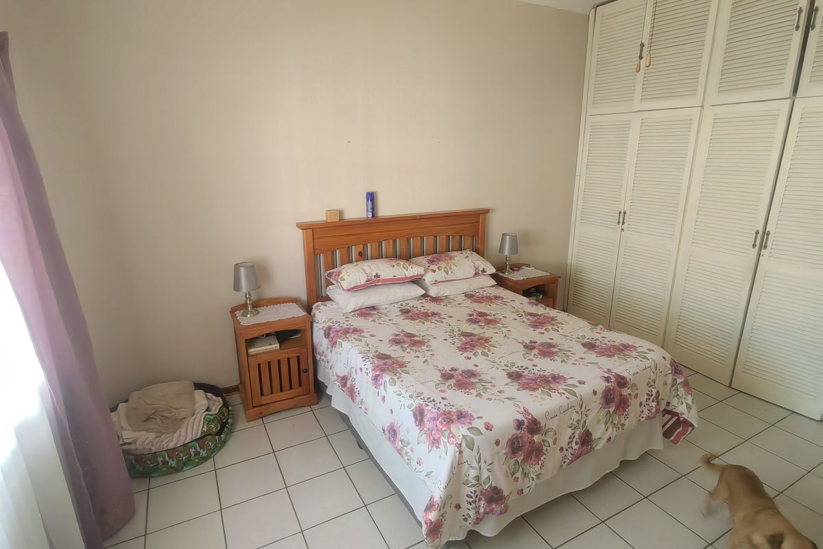 A bedroom featuring tiled flooring, built-in cupboards with louvered doors, and a ceiling fan.