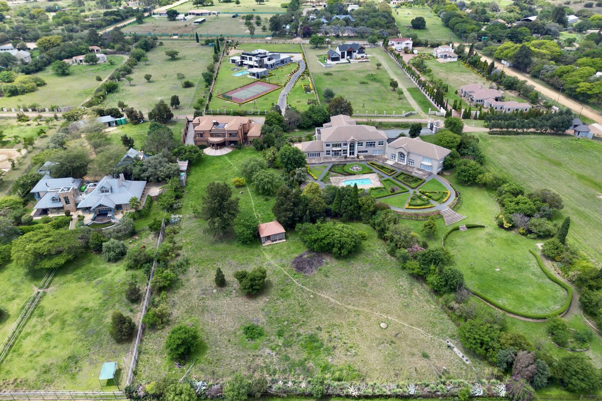 Aerial view of a large residential property featuring extensive landscaped gardens, a swimming pool, and multiple outbuildings within a spacious estate setting.
