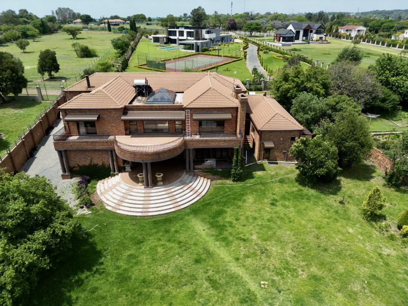 Aerial view of a large brick residence featuring a tiled roof, expansive lawn, and a semi-circular patio area.