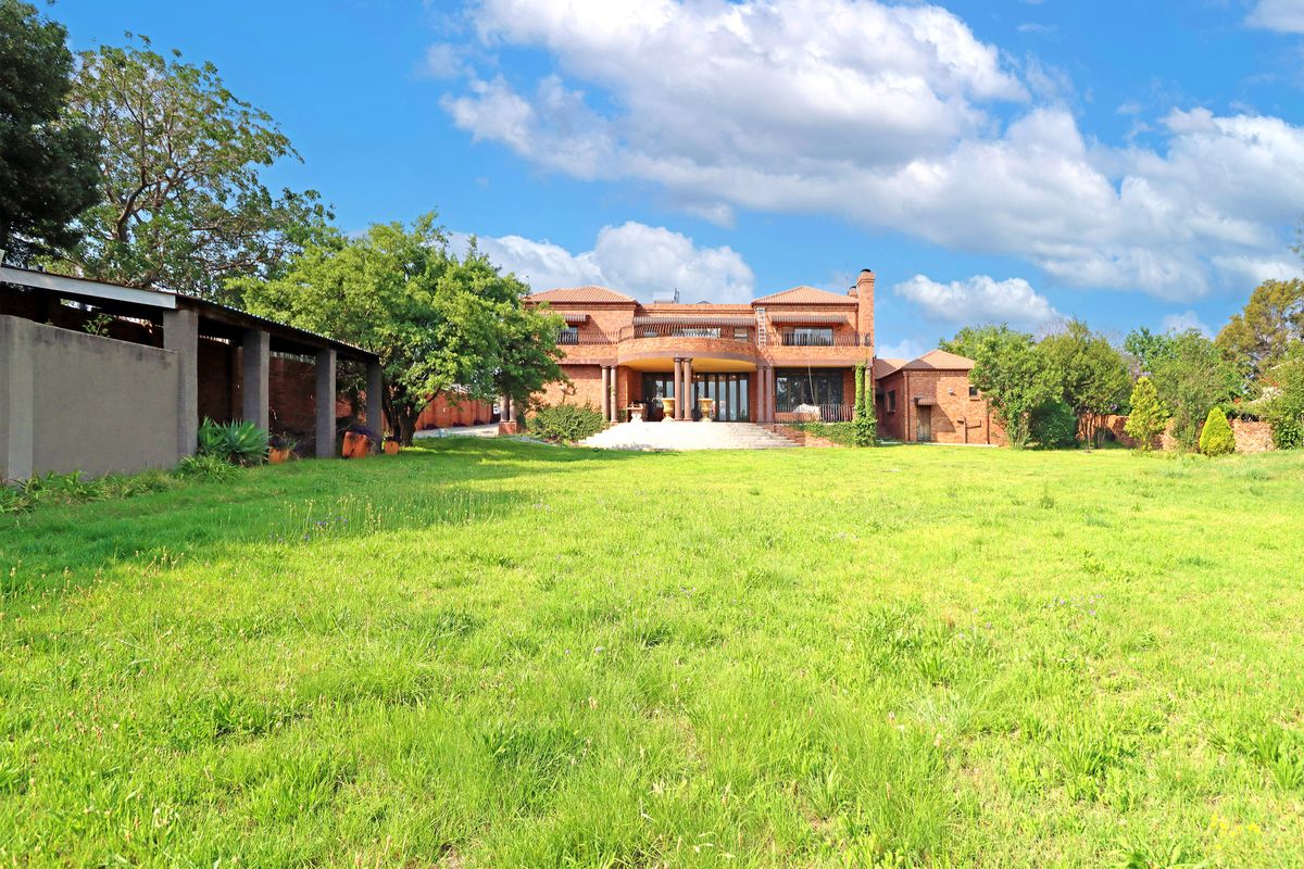 A spacious rear view of a large brick-faced house featuring a prominent balcony, covered patio area, and expansive lawn.