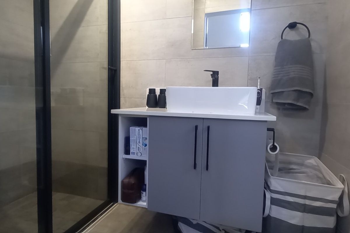 Modern bathroom featuring a floating vanity with a vessel sink, black fixtures, and a glass-enclosed shower with neutral wall tiling.