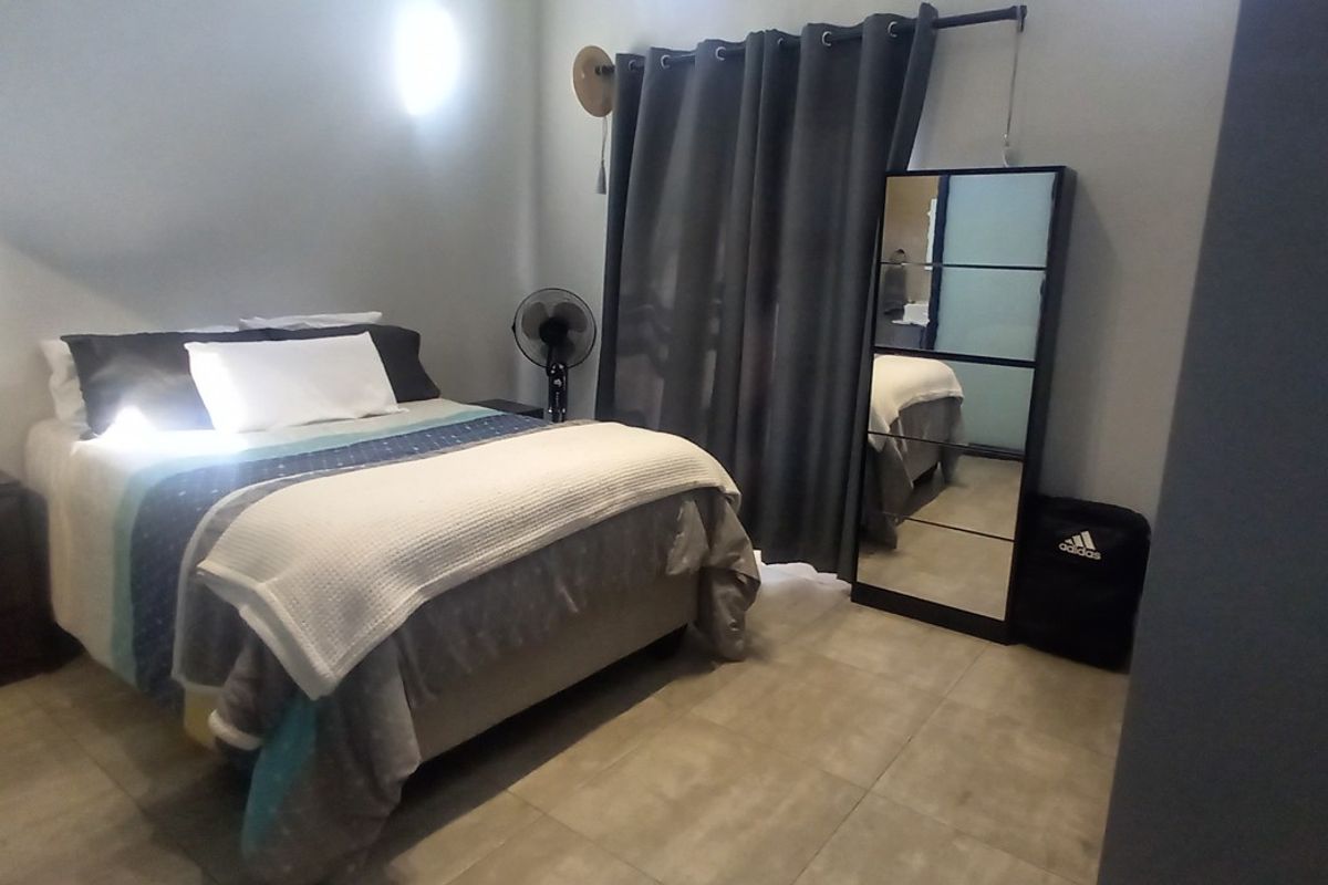 A bedroom featuring neutral tiled flooring and a window dressed with dark curtains.
