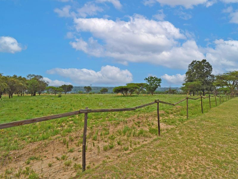 A view of a vacant residential plot featuring open grassy terrain, mature trees, and existing wire and wooden post perimeter fencing.