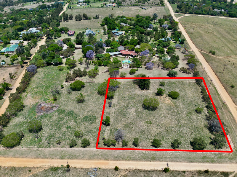 Aerial view of a vacant residential plot featuring established trees and perimeter fencing, situated in a semi-rural neighborhood setting.