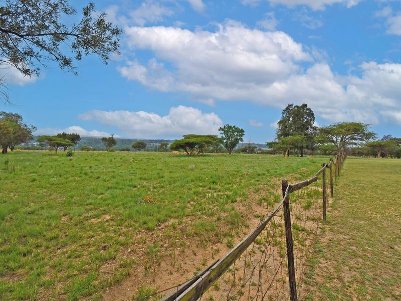 A view of a vacant residential plot featuring open grassland and perimeter wire fencing with wooden posts.