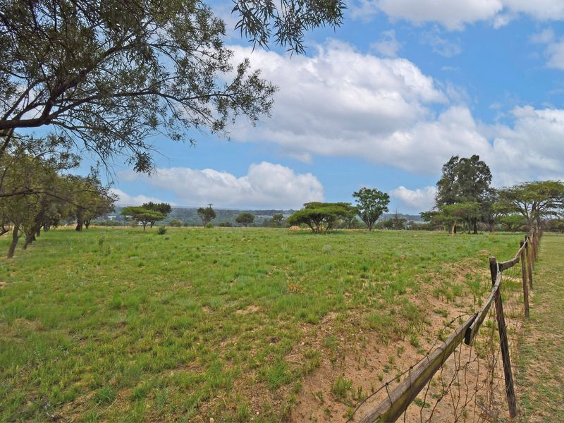 A wide-angle view of a vacant residential plot featuring established trees, natural grassland, and perimeter wire fencing.