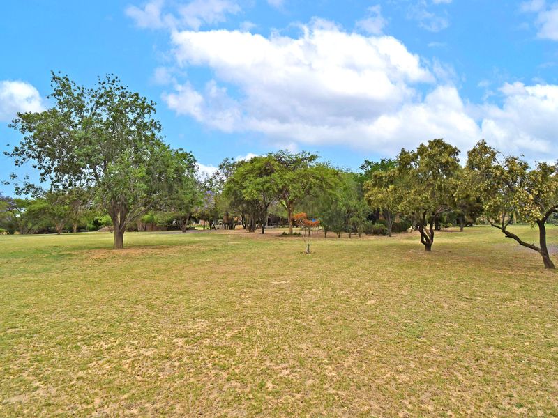 A spacious, well-maintained residential garden featuring established mature trees and an expansive grass lawn area.