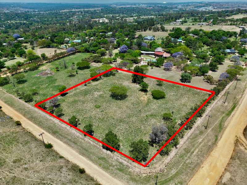 Aerial view of a vacant residential plot featuring established trees and perimeter fencing, situated in a semi-rural neighborhood setting.