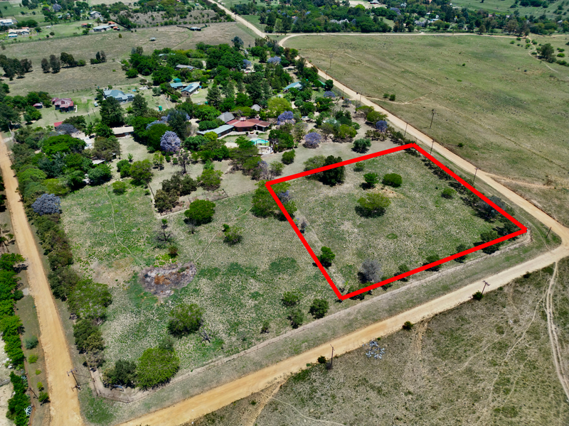Aerial view of a vacant residential plot outlined in red, situated in a rural setting with dirt road access.
