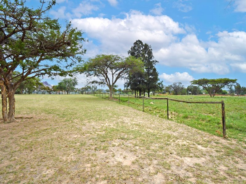 A view of a vacant residential plot featuring open grassy areas, mature trees, and perimeter wire fencing.