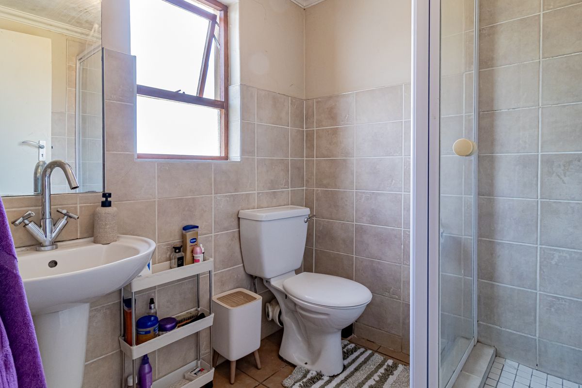 A functional bathroom featuring a pedestal basin, toilet, and a glass-enclosed shower with neutral wall and floor tiling.