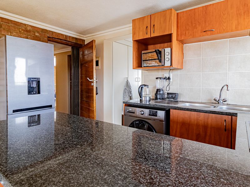 Compact kitchen featuring granite countertops, exposed brick wall detailing, and functional built-in cabinetry with a tiled backsplash.