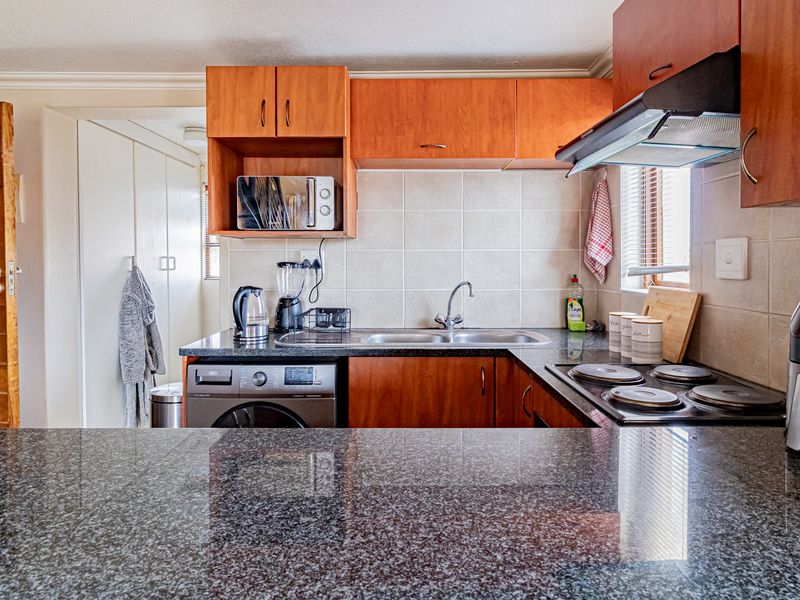 Functional kitchen featuring granite countertops, wooden cabinetry, built-in electric hob, extractor fan, and integrated laundry appliance space.