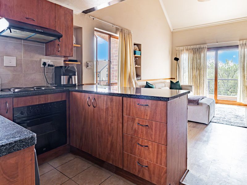 Open-plan kitchen and living area featuring wood-finish cabinetry, granite countertops, vaulted ceilings, and direct access to a balcony through sliding glass doors.
