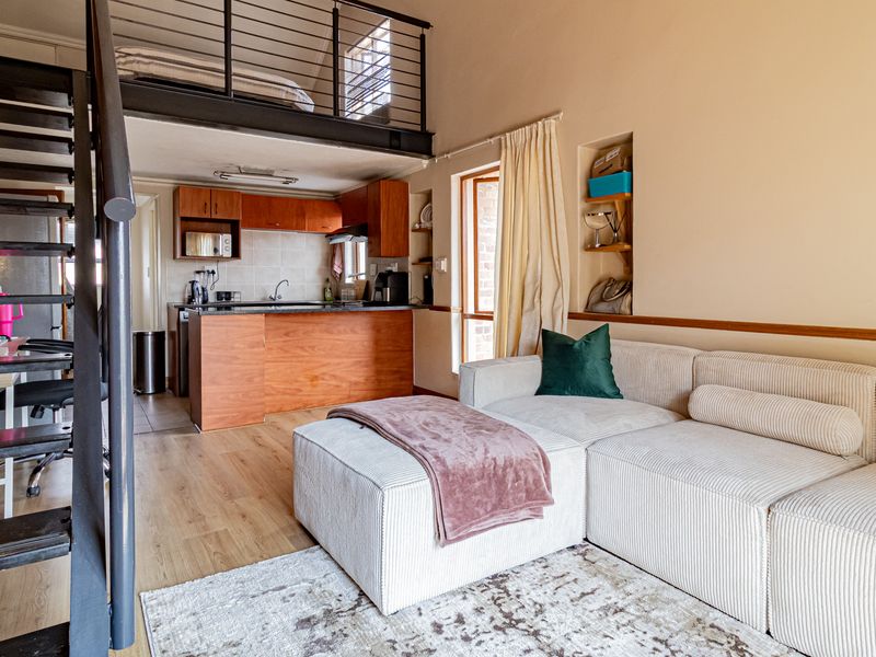 Open-plan living area featuring a mezzanine level, metal staircase, and a functional kitchen with built-in cabinetry and laminate flooring.