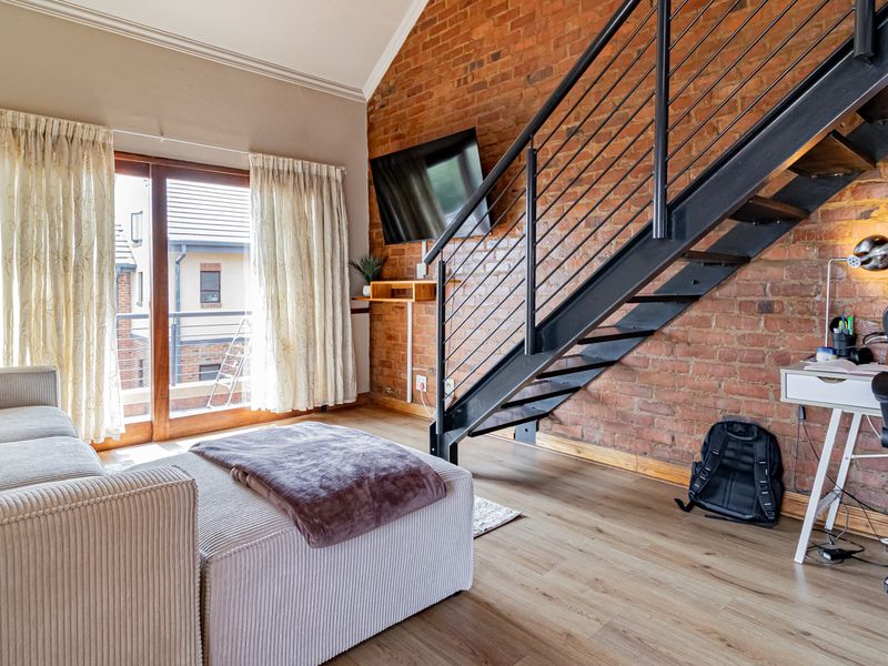 A bright living room featuring an exposed brick wall, vaulted ceiling, and a modern metal staircase leading to an upper level.