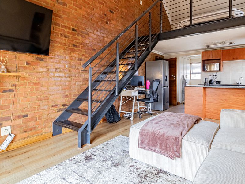 Open-plan living area featuring an exposed brick wall, a modern metal staircase leading to a mezzanine level, and an integrated kitchen space.