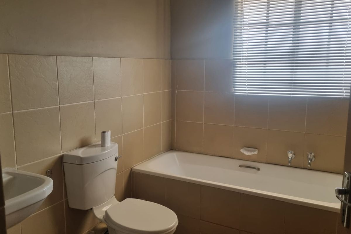A functional bathroom featuring a bathtub, wall-mounted basin, and toilet, finished with neutral wall tiling and fitted with venetian blinds.