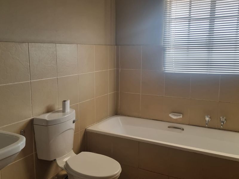 A functional bathroom featuring a bathtub, wall-mounted basin, and toilet, finished with neutral wall tiling and fitted with venetian blinds.