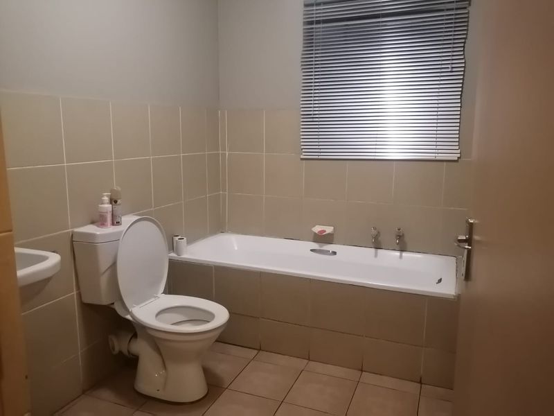 A functional bathroom featuring a built-in bathtub, toilet, and basin with neutral wall and floor tiling.